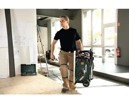 Muž prepravuje stolovú pílu Metabo v zloženom stave.