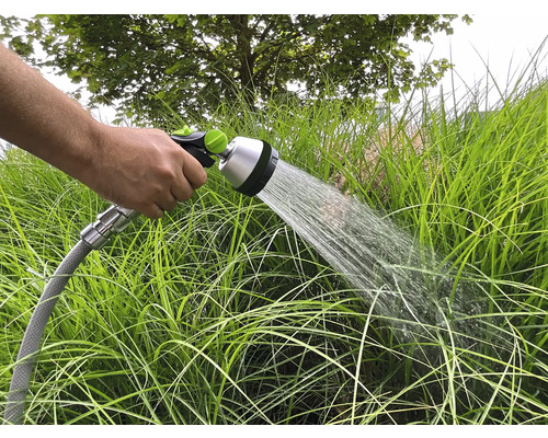 Ruka drží záhradnú hadicu, ktorou sa zavlažujú záhradné rastliny.
