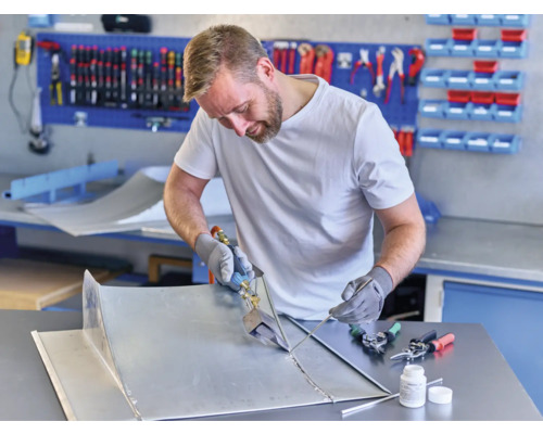 Remeselník spájkuje kovové diely v dielni s nástrojmi a pracovným stolom