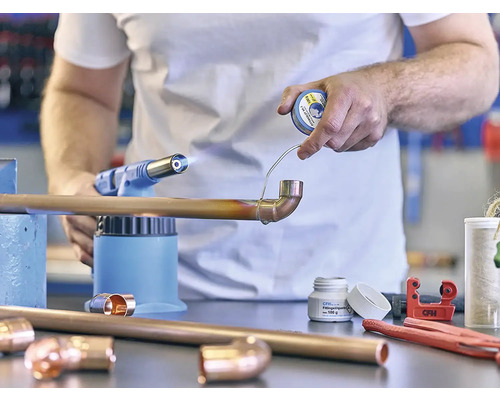 Remeselník spájkuje medenú rúrku s spájkovacou lampou a spájkou