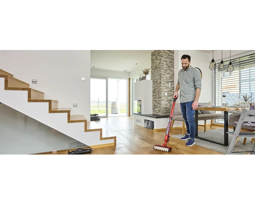 Muž čistí drevenú podlahu pomocou akumulátorového mopu s vysávačom v modernom obývacom priestore
