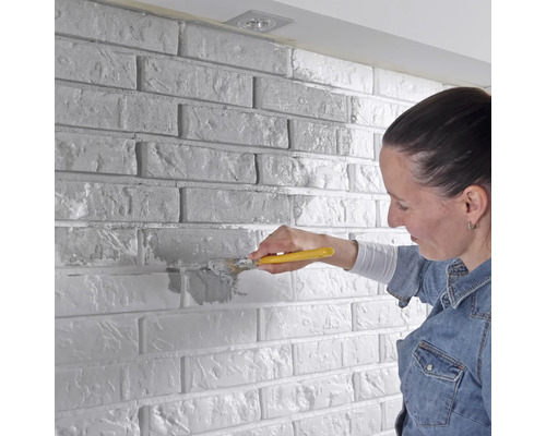 Žena natiera tehlovú stenu štetcom