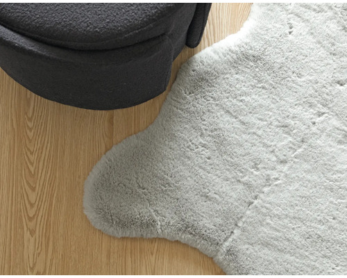 Detailný pohľad na sivý koberec so vzhľadom ovčej kože vedľa kresla na drevenej podlahe