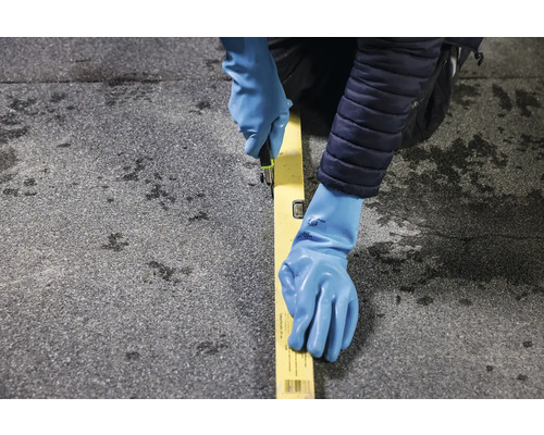 Osoba v rukaviciach reže nožom pozdĺž vodováhy na povrchu.