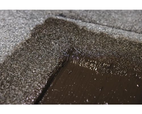 Detailný záber opravy strechy s asfaltovou hmotou.