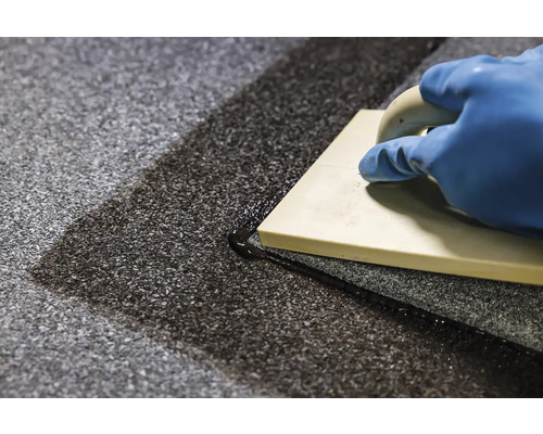 Ruka v rukavici a škárovacia hladítka pri škárovaní podlahových dlaždíc