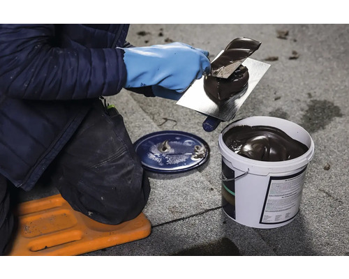 Pokrývač nanáša špachtľou hmotu na hydroizoláciu strechy z vedra