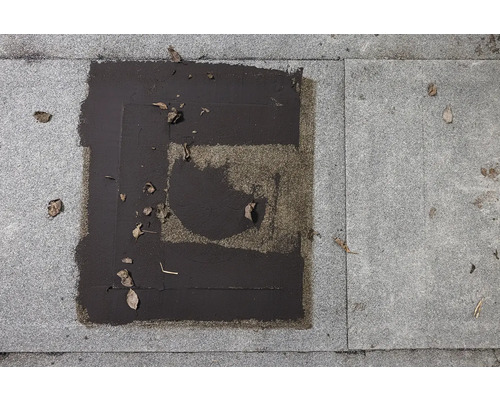 Detailný záber dlažby s bitúmenovými záplatami a lístím