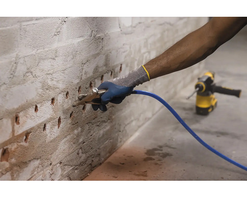 Osoba čistí vŕtané otvory v tehlovej stene ofukovacou pištoľou v rámci prípravy na opravy.