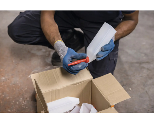 Osoba pripevňuje červenú výlevku k prázdnej fľaši nad kartónovou krabicou.