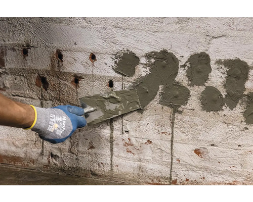 Osoba vypĺňa špachtľou otvory v tehlovej stene.