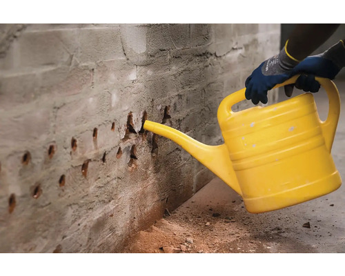 Osoba kropí tehlovú stenu žltou kanvou, aby sa viazal prach.