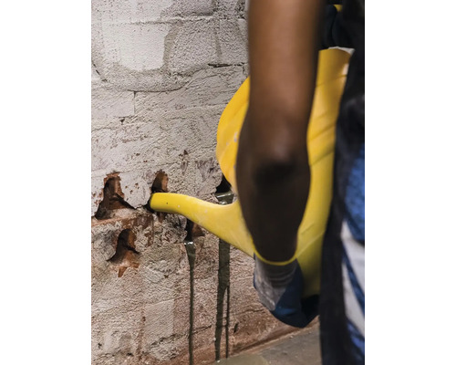 Osoba nalieva tekutinu z kanvy do poškodenej tehlovej steny.