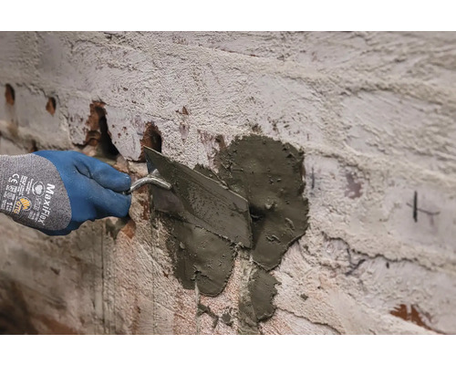 Ruka v rukavici nanáša maltu na stenu pomocou lyžice.