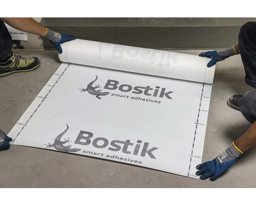 Osoby rozbaľujú fóliu s inteligentným lepidlom Bostik na podlahe.