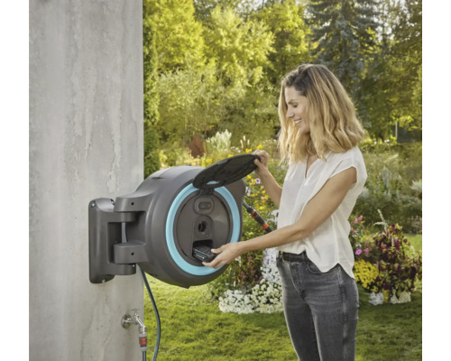 Žena obsluhuje navijak na hadicu Gardena namontovaný na stene v záhrade.