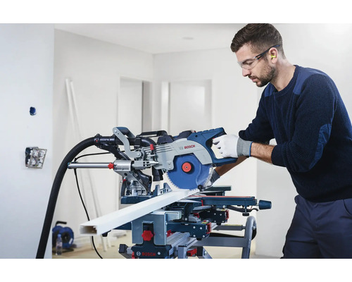 Muž s ochrannými okuliarmi a chráničmi sluchu používa pokosovú pílu Bosch na rezanie obrobku