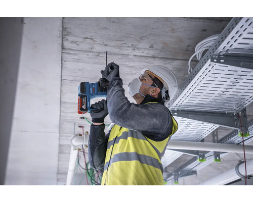 Remeselník vŕta do stropu vŕtacím kladivom.