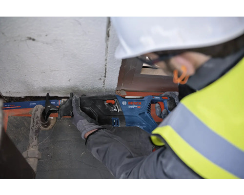 Muž s ochrannou prilbou reže rúru pílkou šabľou Bosch.