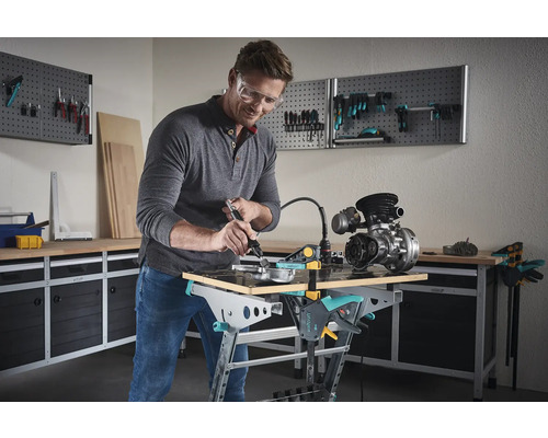 Muž pracuje s multifunkčným nástrojom na obrobku na ponku v dielni.