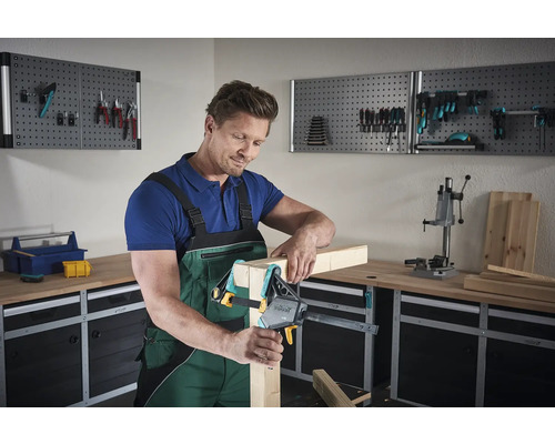 Muž upevňuje kusy dreva jednou rukou v dielni.