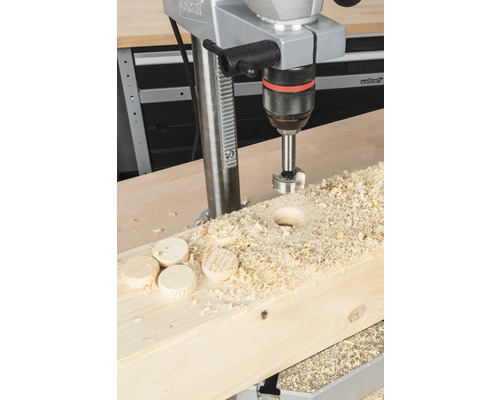 Stojanová vŕtačka vŕta otvor do drevenej dosky s drevenými štiepkami a drevenými diskami