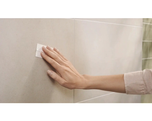 Ruka pritláča obojstrannú lepiacu pásku na dlaždice