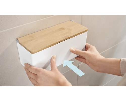 Snímka osoby pripevňujúcej biely box na kozmetické vreckovky s bambusovým vekom na stenu.