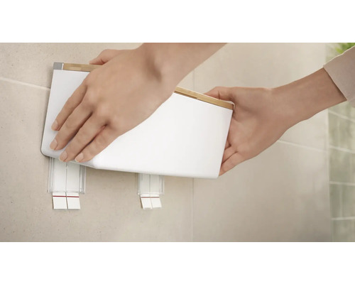 Osoba pripevňuje dávkovač mydla na nástenný držiak.