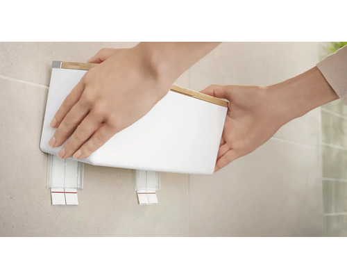 Osoba pripevňuje biely nástenný dávkovač mydla s bambusovým vekom na stenu