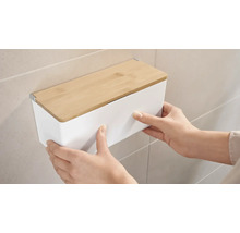 Osoba montuje biely nástenný box s bambusovým vekom na stenu