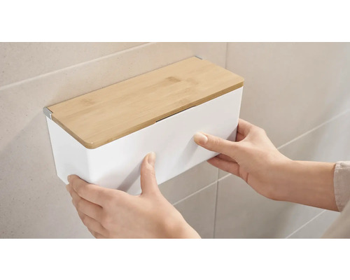 Osoba montuje biely nástenný box s bambusovým vekom na stenu