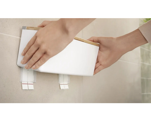 Osoba pripevňuje bielu nástennú kozmetickú nádobu s bambusovým vekom na stenu