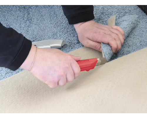 Dve ruky režú koberec kobercovým nožom.