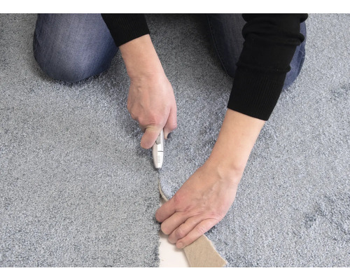 Osoba reže koberec pomocou kobercového noža.