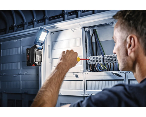 Elektrikár pracuje na rozvodnej skrini s pracovným svetlom Bosch.