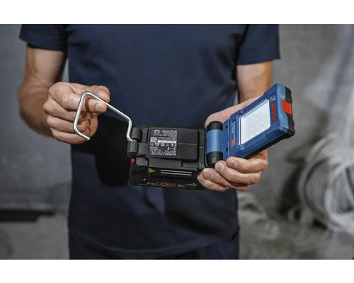 Muž drží akumulátorové pracovné svetlo s hákom značky Bosch.