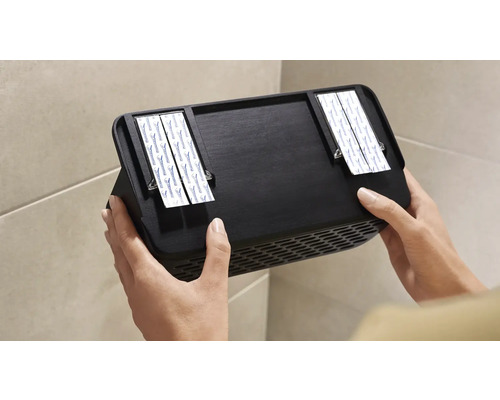 Osoba pripevňuje čierny nástenný ventilátor pomocou lepiacich prúžkov na stenu