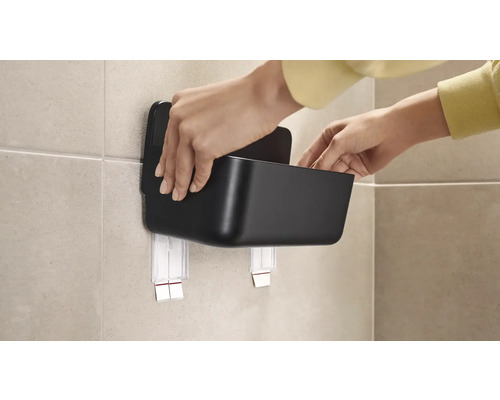 Osoba pripevňuje čierny úložný box pomocou lepiacej upevňovacej súpravy na stenu.