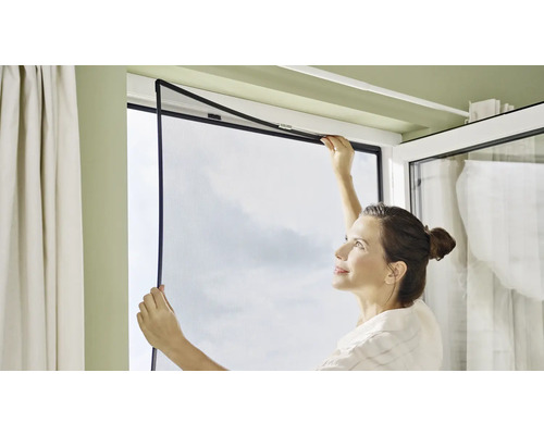 Žena montuje do okna sieť proti hmyzu.