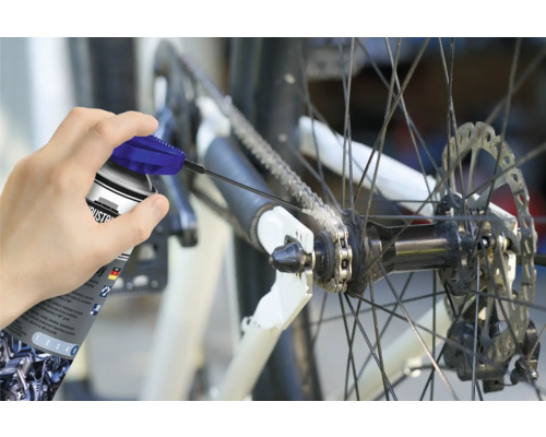 Osoba maže reťaz bicykla sprejom na reťaze.