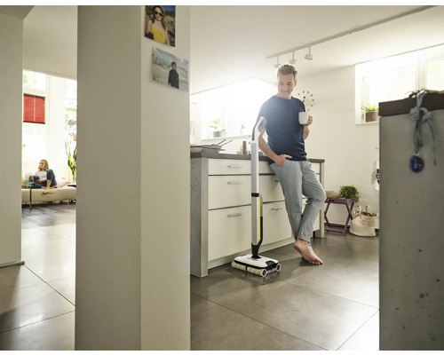 Muž sa opiera o kuchynskú linku so šálkou v ruke vedľa elektrického mopu.