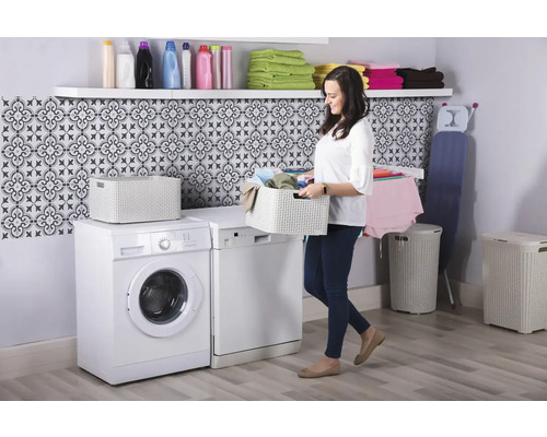 Svetlá práčovňa s práčkou, sušičkou, košom na bielizeň, truhlicou na bielizeň, policou a ženou nesúcou kôš na bielizeň.