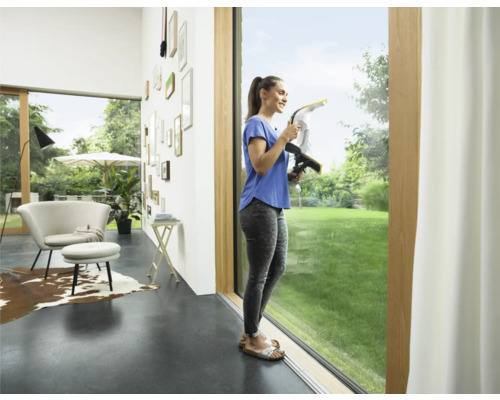 Žena čistí okná pomocou okenného vysávača v jasnej obývacej izbe.