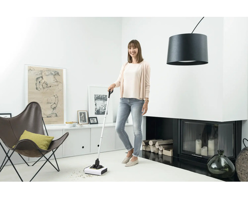 Žena používa akumulátorovú metlu na upratovanie v obývacej izbe.