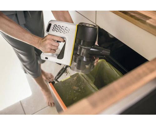 Osoba vysýpa akumulátorový vysávač nad odpadkový kôš.