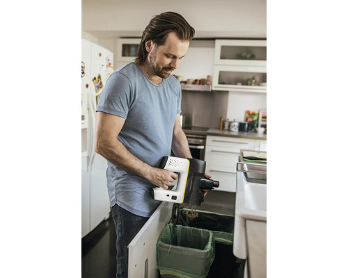 Muž vysýpa ručný vysávač nad odpadkový kôš v kuchyni.