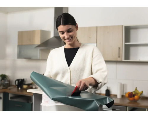 Žena nanáša dekoratívnu fóliu stierkou v kuchyni