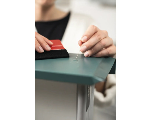 Osoba odstraňuje bubliny zo samolepiacej fólie pomocou ihly a stierky.