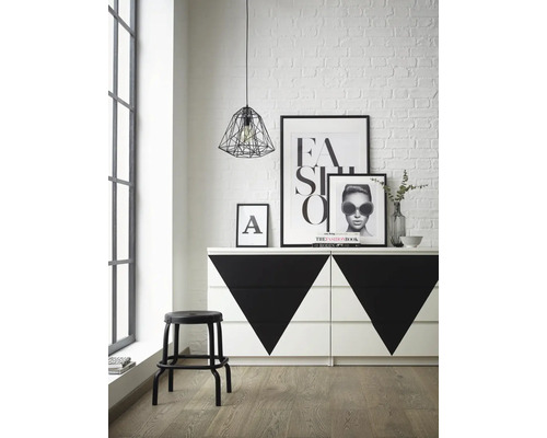 Interiérová fotografia miestnosti s komodou s geometrickými vzormi, stoličkou, plagátmi a závesným svietidlom.